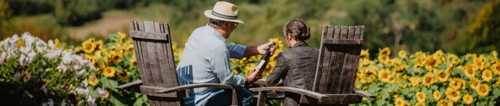 Couple dans la cinquantaine qui partage une bouteille de vin assis sur des chaises de bois rustiques aux abords d'un champ de Tournesols
